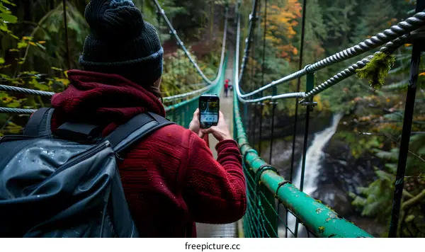Man Taking a Photo of Waterfall on Suspension Bridge