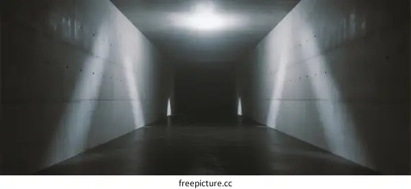 A dark and narrow concrete corridor with light beams coming in