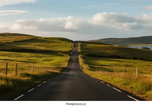 A long straight road stretching through green countryside with clear sky
