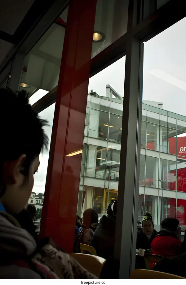 People Sitting In Cafe Looking Out Of Window At Modern Building