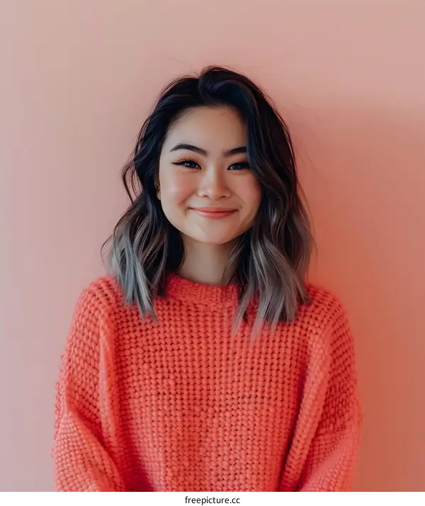 Smiling Asian Woman in Pink Sweater Against a Coral Wall