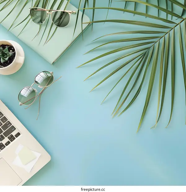 Laptop, Sunglasses, Notebook and Palm Leaves on Blue Background