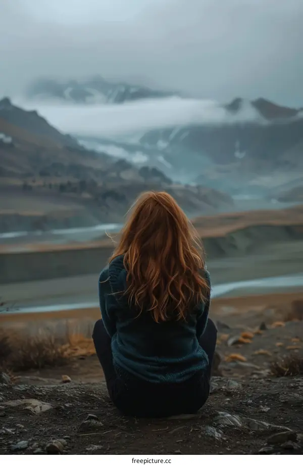 girl sitting on the edge of a cliff looking at a mountain range