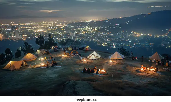 A group of people camping on a hilltop overlooking a city at night