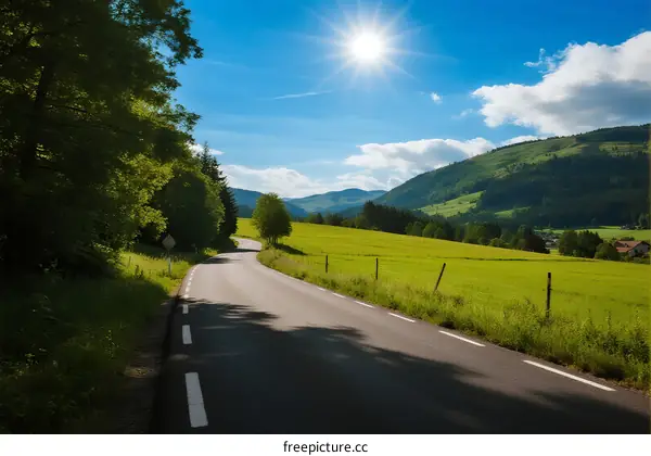 Sunny country road with green fields and mountains in the distance