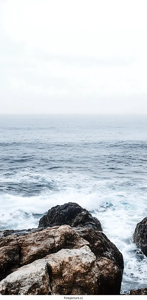 Ocean Waves Crashing On Rocks With Foggy Sky