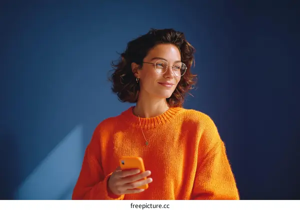 Woman Holding Smartphone in Orange Sweater Against Blue Background
