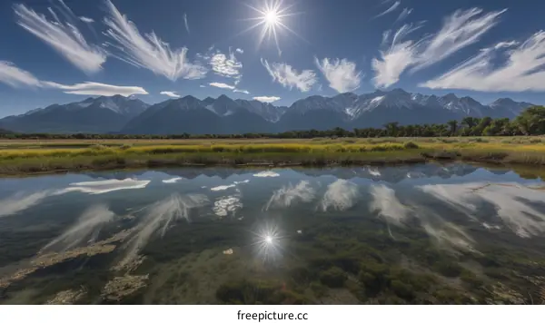 The sun shines through the clouds over the mountains and reflects on the lake