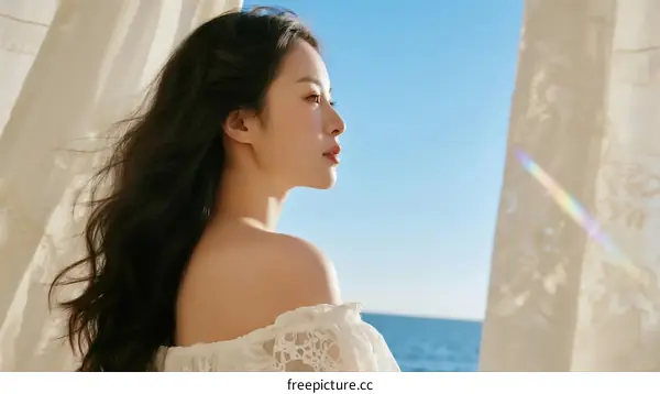 A woman with long black hair stands by the sea