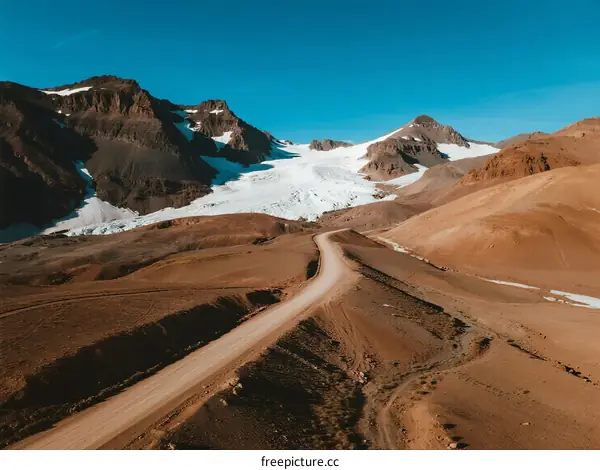 Winding dirt road through arid mountainous terrain with snow