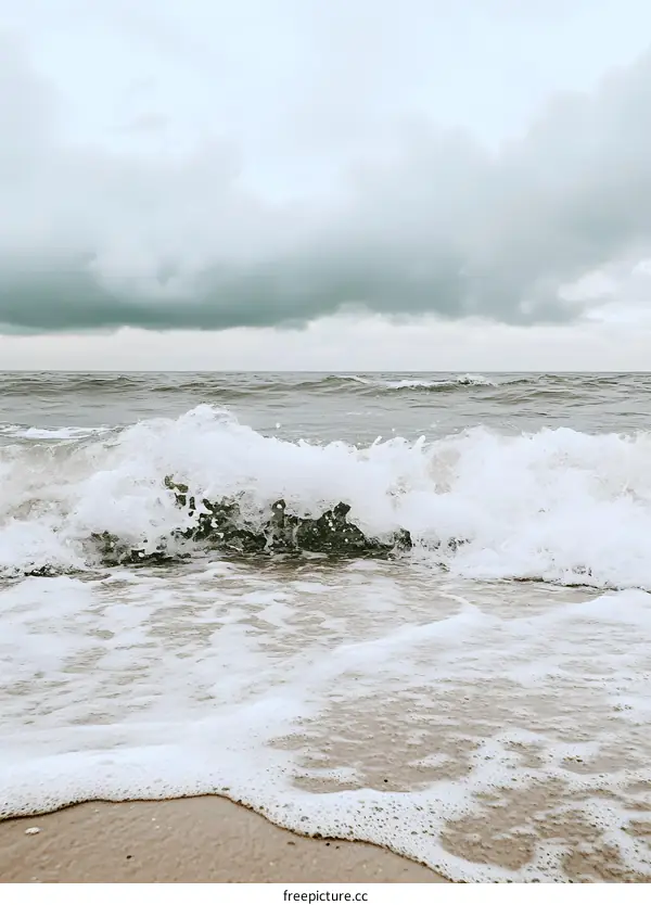 White Waves Crashing on Sandy Beach Under Cloudy Sky