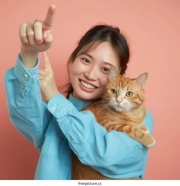 A young Asian woman is holding an orange cat and pointing with her finger