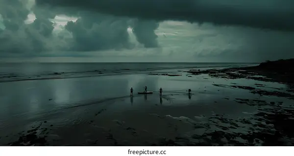 Silhouettes of People Walking on the Beach with a Boat at Low Tide Under a Cloudy Sky