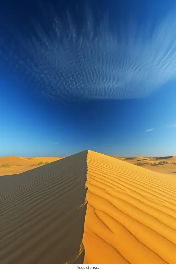A large sand dune in the middle of a desert with a blue sky and wispy clouds