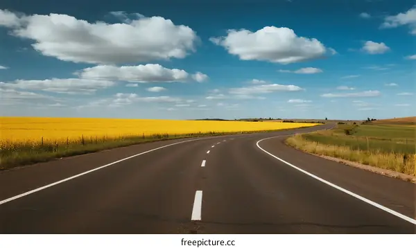 A long straight road stretching through a vast field under a clear blue sky