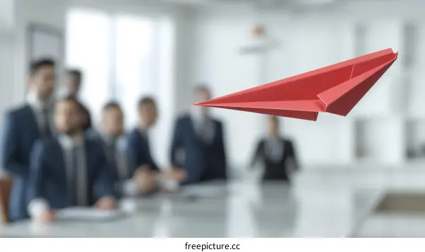 Red paper plane flying in a modern office with a group of business people in the background