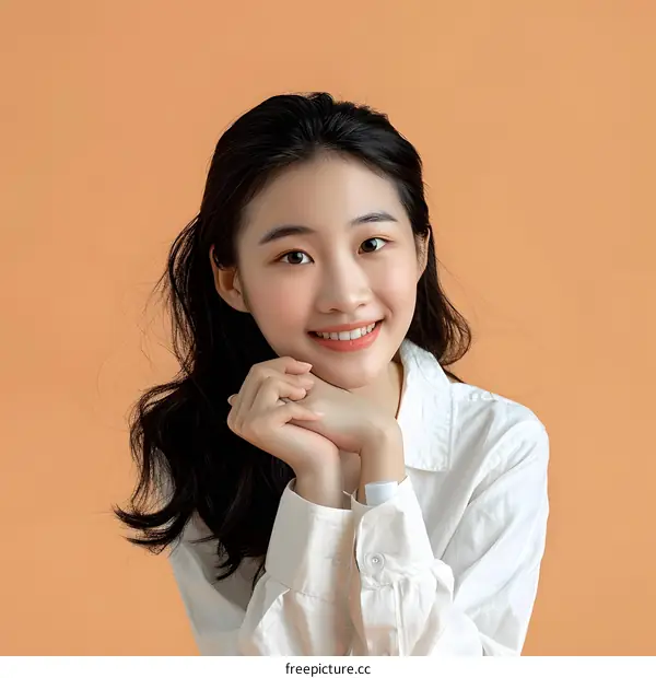 Portrait of a Young Asian Woman Smiling in a White Shirt Against a Peach Background