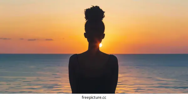 Young African woman watching the sunset over the ocean