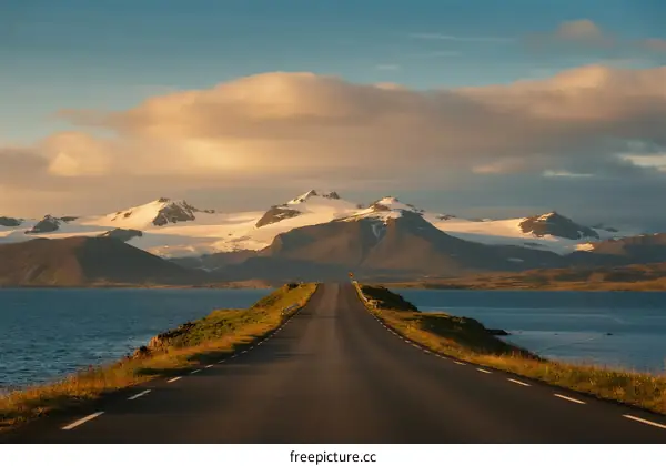 Scenic road leading to snow-capped mountains under a cloudy sky