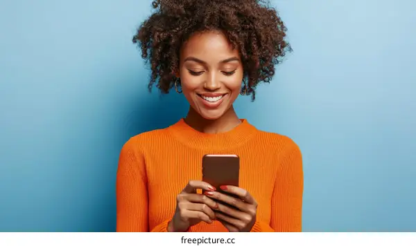 Smiling Woman Using Smartphone in Orange Sweater