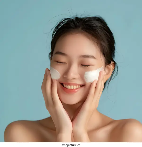 Happy Asian Woman Applying Face Cream with Closed Eyes