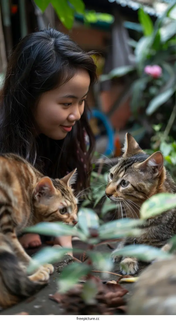 A young woman is petting two cats in a garden.